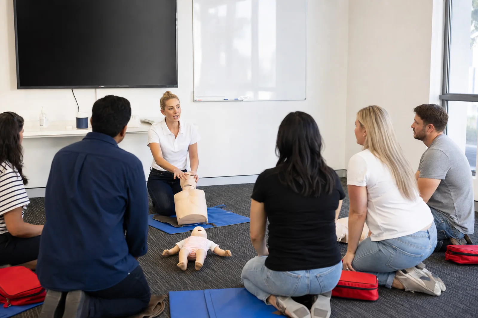 A trainer guiding a learner through chest compressions on a CPR manikin